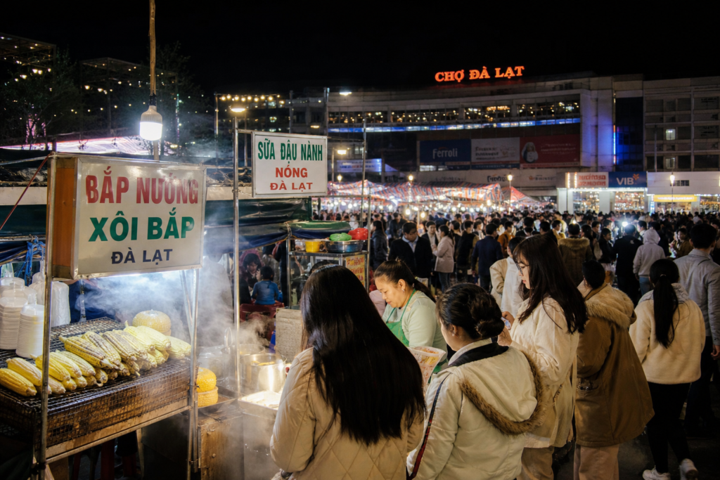 Da Lat night market in Vietnam with bustling food stalls, warm string lights, and steam rising from grilled corn stands in the cool mountain evening