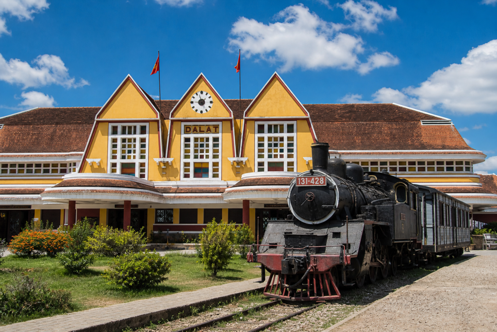 Da Lat Railway Station in Vietnam with distinctive yellow French colonial art deco architecture and an old steam train parked outside