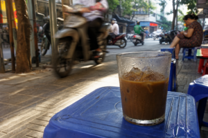 Glass of ca phe sua da sweating on a blue plastic stool on a Hanoi sidewalk