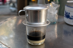 Vietnamese phin filter dripping dark coffee onto condensed milk in a small glass