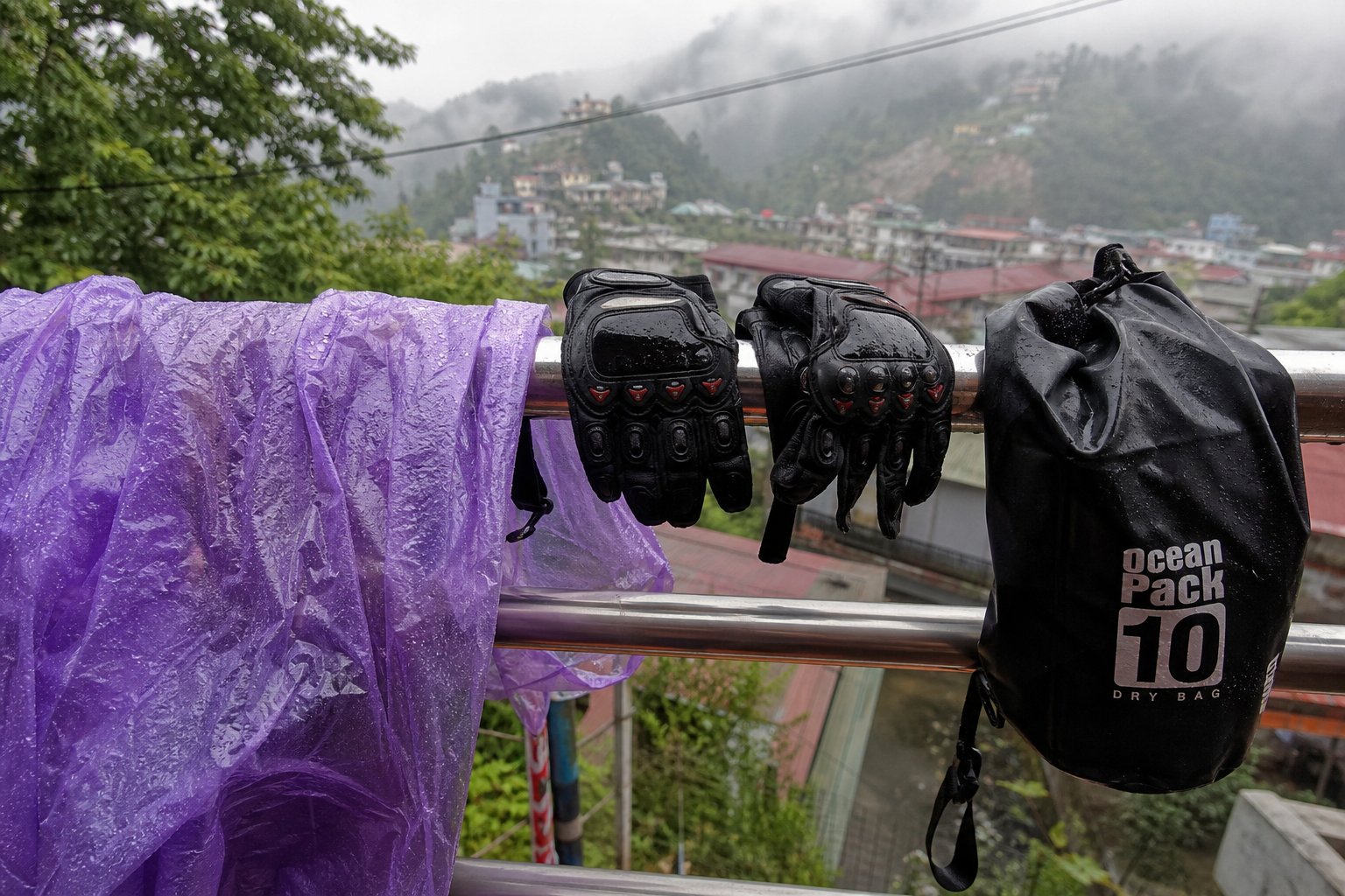 Plastic rain poncho, motorbike gloves and dry bag drying on a balcony railing in a misty Vietnamese mountain town