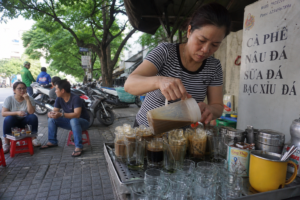 Busy Vietnamese sidewalk coffee stall with rows of glasses and low plastic stools