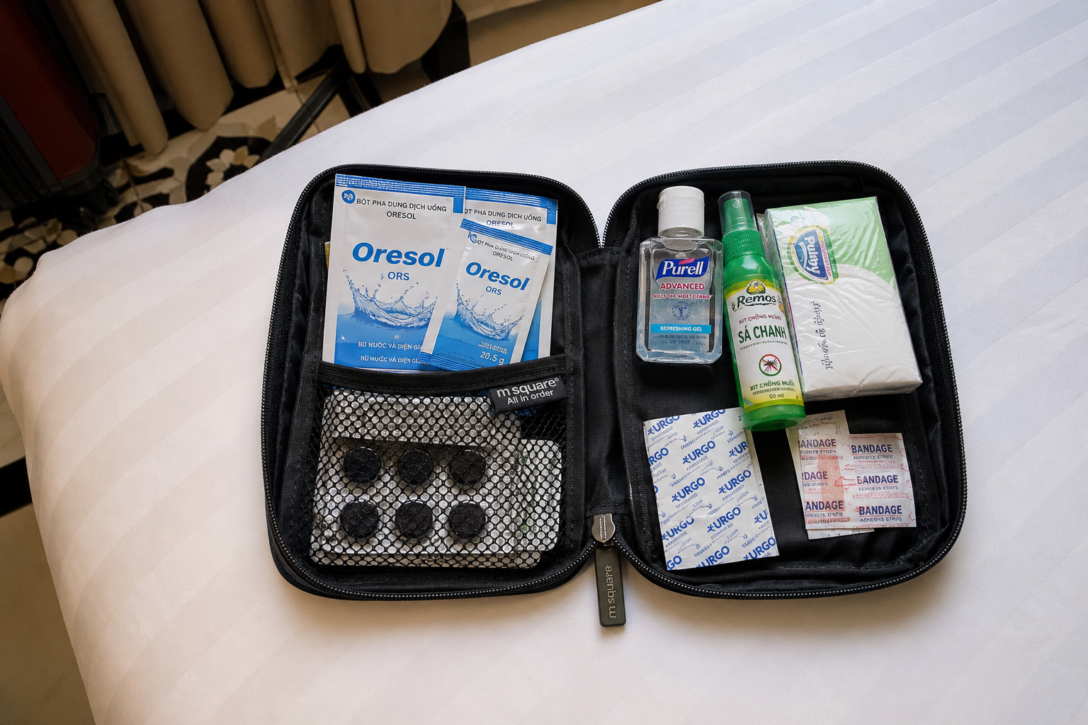 Small travel medicine pouch with rehydration salts, charcoal tablets, sanitiser, tissues and insect repellent on a hotel bed