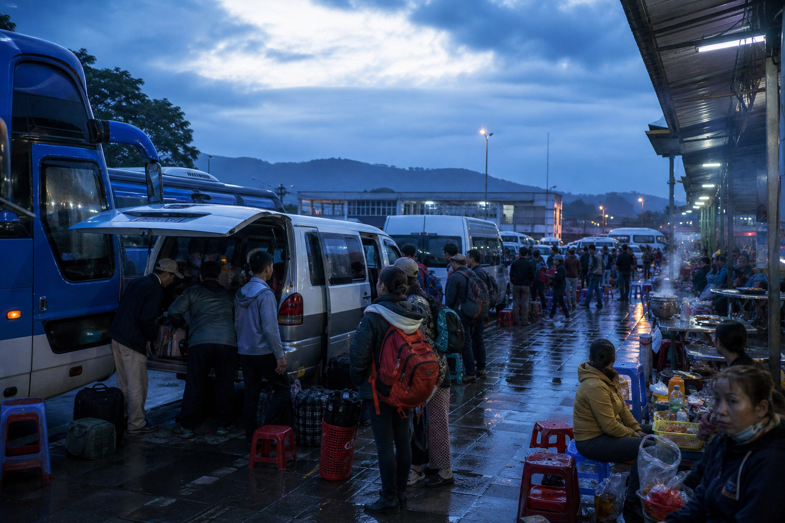 Travellers waiting with backpacks at a Vietnamese bus station at dawn as drivers load luggage into coaches