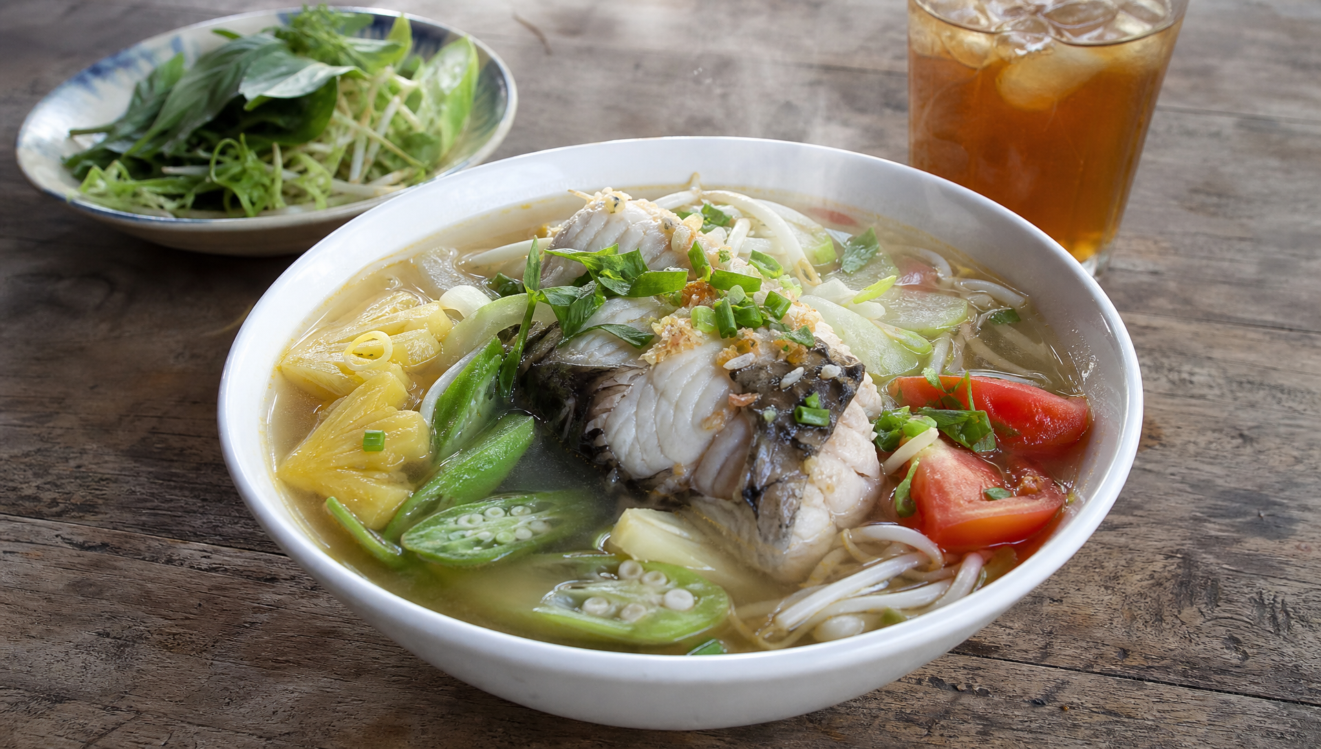 Bowl of Vietnamese sour soup with snakehead fish, tomato, pineapple, okra and rice paddy herb in a tamarind broth