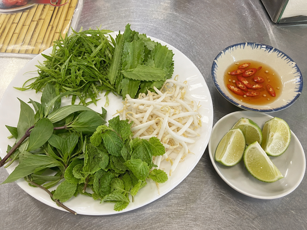 Plate of fresh herbs with bean sprouts beside a small dish of fish sauce with sliced chilli