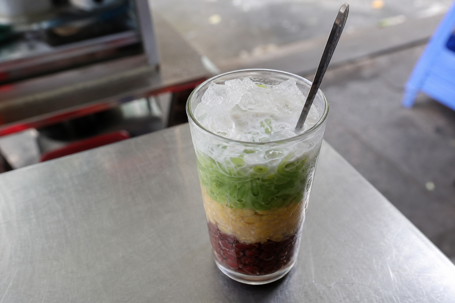 Glass of chè ba màu with layers of red bean, mung bean and pandan jelly under crushed ice and coconut milk