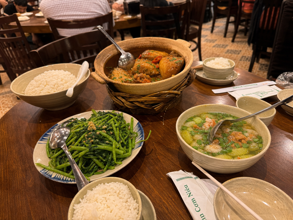 A round table at a Vietnamese restaurant covered with shared dishes, rice bowls, and serving spoons