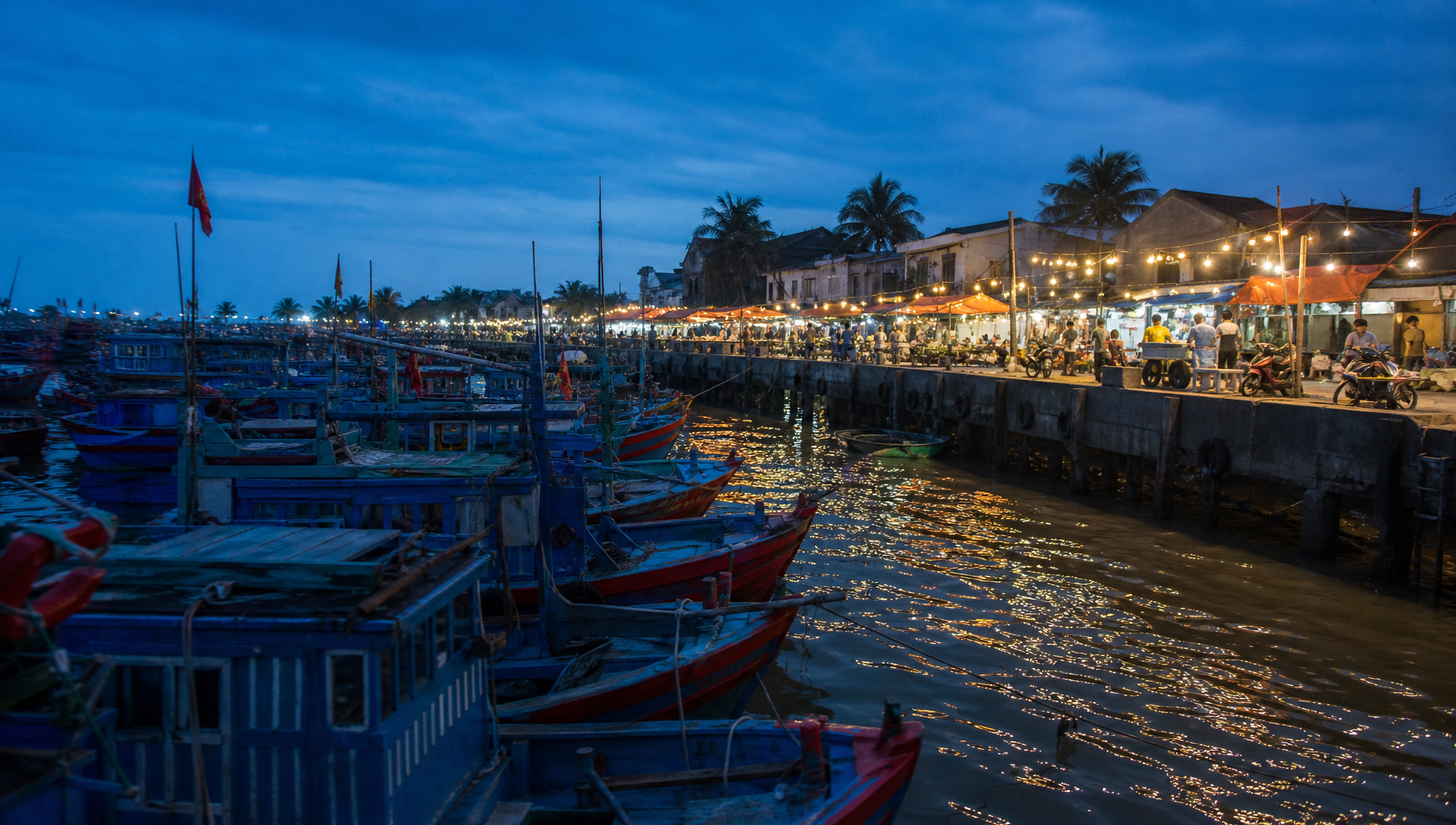 Fishing boats lined up along the harbor in Duong Dong town at dusk, with market lights glowing along the waterfront