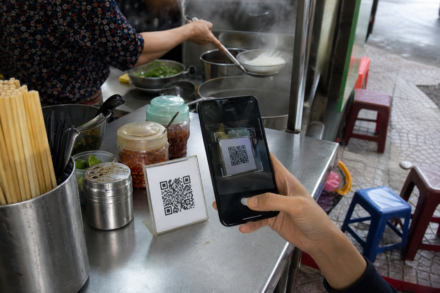 Laminated QR payment code standing on a Vietnamese street food stall counter as a customer scans it with a phone