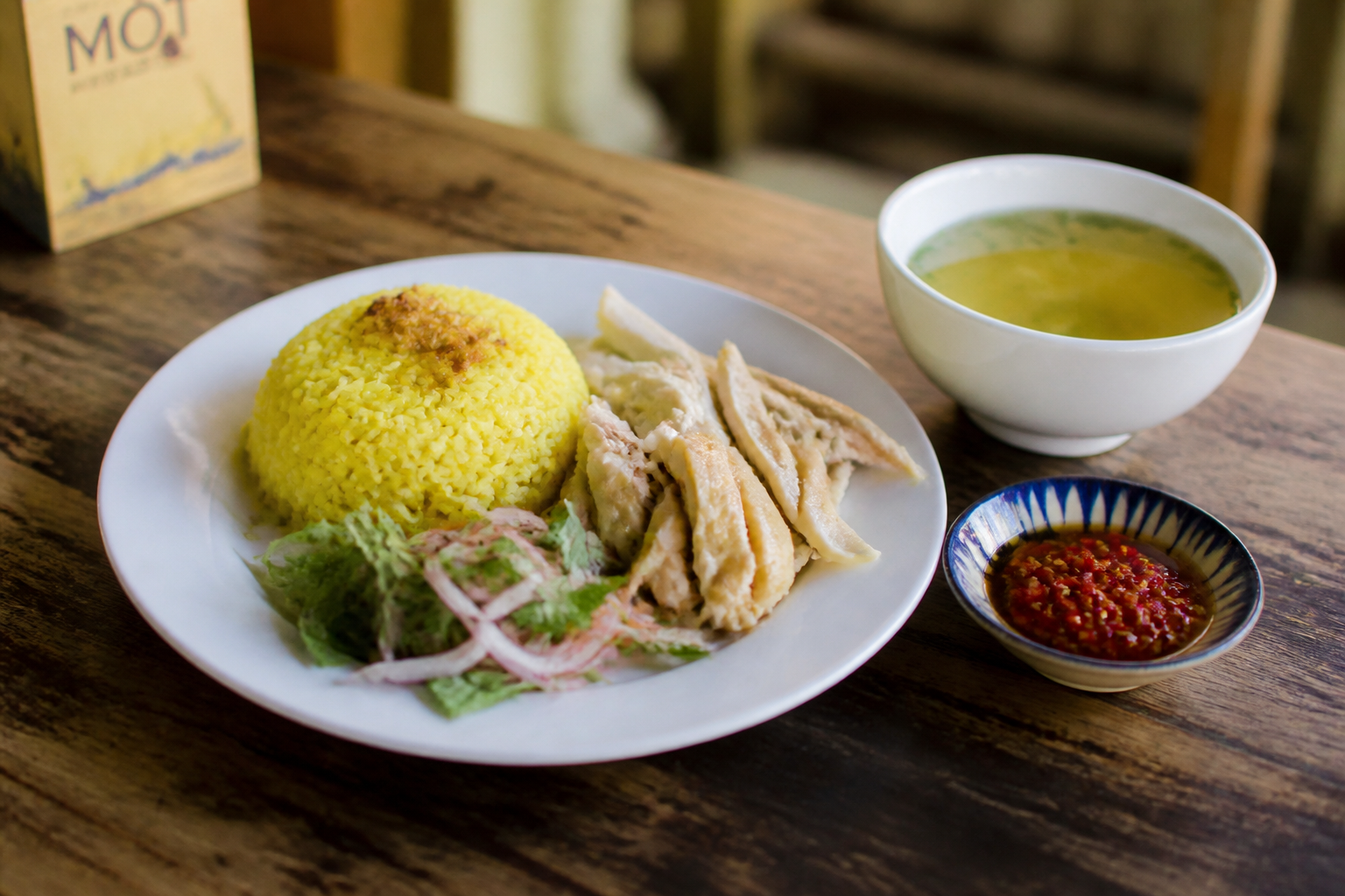 Plate of Hoi An chicken rice with yellow rice, shredded chicken, pickled onion and herbs beside a bowl of broth