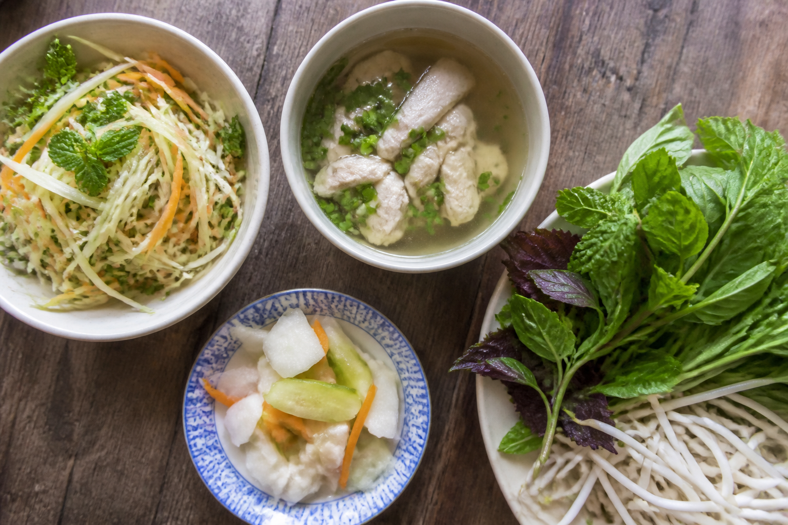 Side dishes for chicken rice: green papaya salad, chicken broth with scallion, pickles and fresh herbs